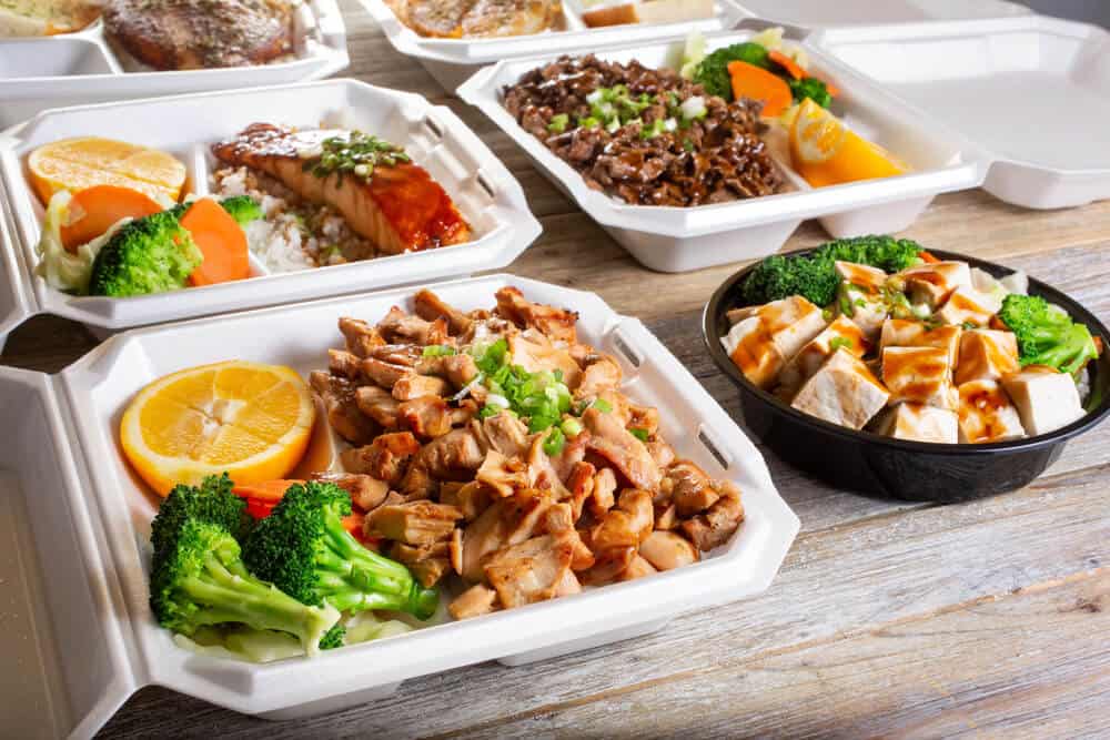 Hot boxed lunch setup with grilled meats, roasted vegetables, and fresh fruit ready to serve at a construction site.